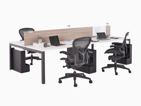 Estación de trabajo con benching Layout Studio y pantallas en el centro laminadas y veteadas en gris, espacio de guardado para bolsos y carteras Ubi, organizadores de escritorio y cuatro sillas Aeron graphite.