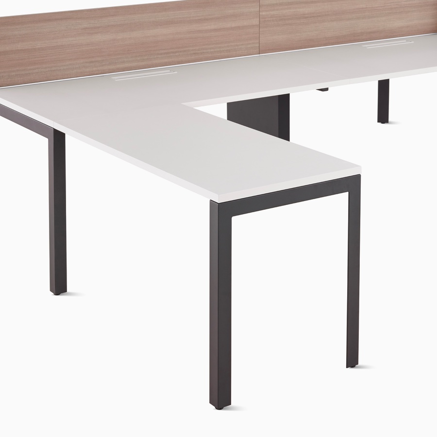 Close-up of a white top, graphite base Layout Studio benching workstation with L-shaped return-end work surface and woodgrain laminate center screen.