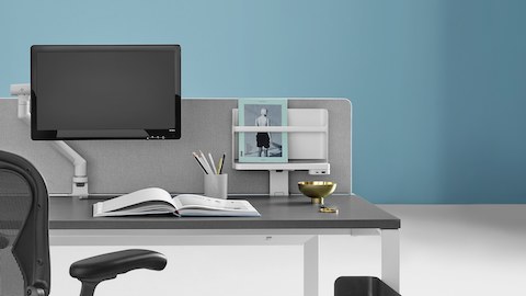 Layout Studio estação de trabalho individual com tampo cinza, uma lapiseira, livro aberto, um Monitor Braço Flo com monitor e uma cadeira Aeron preta.