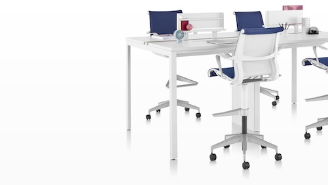 A standing-height Layout Studio benching workstation with white desk top and blue upholstered Setu Stools.