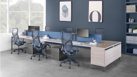 Six-person Layout Studio bench with a blue divider screen and attached credenza, dark blue Cosm chairs and under desk storage.