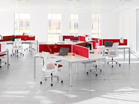 An open office featuring curved Layout Studio work surfaces with red privacy screens and white Sayl office chairs with red seats.