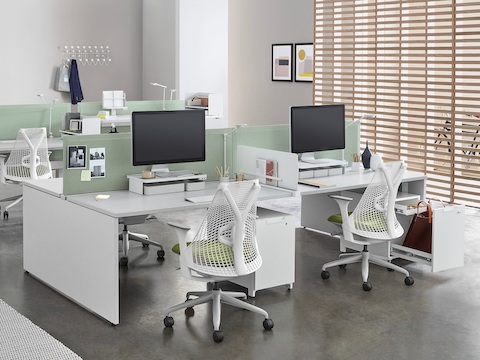 An office setting with two white, four-pack Layout Studio bench that has green fabric, center privacy screens, Sayl Chairs, and Tu Wood pedestals.