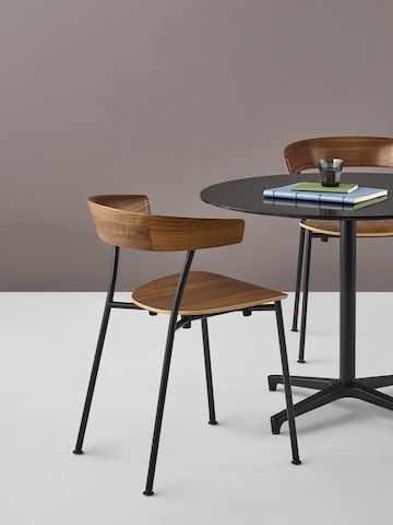 Two Leeway Chairs with black metal bases and dark wood seats and backs at a black Saiba table with a coffee cup and notebooks on top.