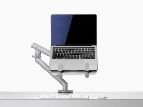 Een open laptop verhoogd en ondersteund door een grijze Ollin-laptopsteun aangesloten op een Flo-monitorarm.