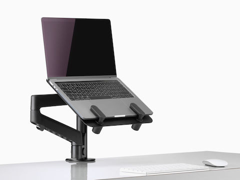 Vista de ângulo lateral de um laptop aberto e elevado de uma mesa, apoiado por um suporte para laptop e um braço para monitor pretos Lima. Vista de ângulo lateral de um laptop aberto e elevado de uma mesa, apoiado por um suporte para laptop e um braço para monitor pretos Lima.