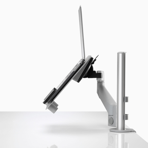Profile view of an open laptop raised and supported by a gray Lima Laptop Mount connected to a Lima Monitor Arm.