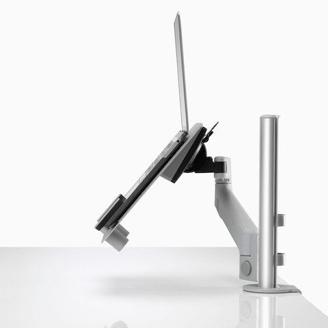 Vista de perfil de um laptop aberto e elevado, apoiado por um suporte para laptop Lima cinza conectado a um braço para monitor Lima. Vista de perfil de um laptop aberto e elevado, apoiado por um suporte para laptop Lima cinza conectado a um braço para monitor Lima.