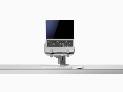 Een open laptop boven een bureau en ondersteund door een grijze Lima-laptopsteun en Lima-monitorarm.