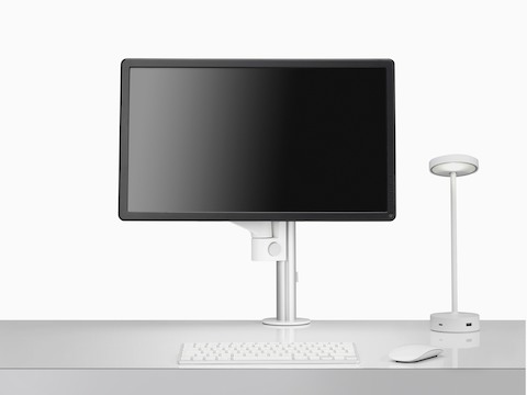 Vista frontale di un braccio porta monitor Lima singolo con luce personale Lolly e tastiera.