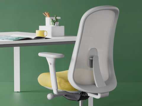 Grauer und gelber Lino Stuhl vor einem Schreibtisch mit Zubehör, schräg von hinten betrachtet.