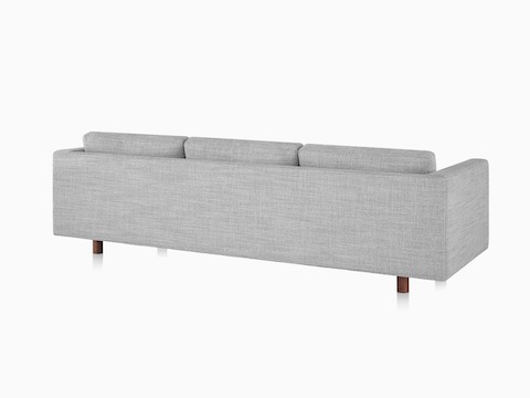 Ein Lispenard Sofa mit Nussbaum-Beinen und grauem Textilbezug, schräg von hinten betrachtet.