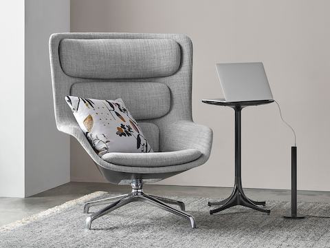 A black Logic Micro Tower placed near a Striad lounge chair and Nelson Pedestal Table. A laptop on the table has its power cord plugged into the Logic Micro Tower. 