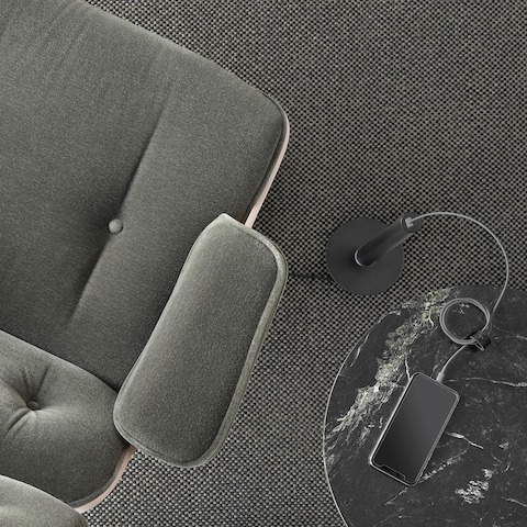 An overhead view of a black Logic Micro Tower placed next to a gray mohair Eames Lounge Chair and black marble-topped Nelson Pedestal Table. A smartphone on the table has its power cord plugged into the Logic Micro Tower.