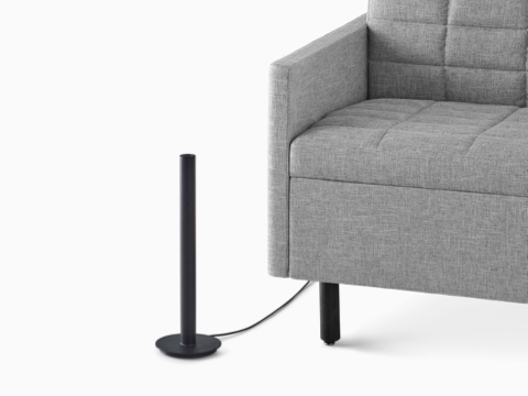 A black Logic Micro Tower placed next to a gray Tuxedo sofa.