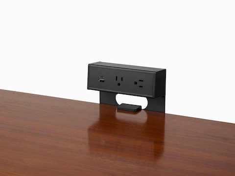Black power source attached to brown wood table with USB-C port, USB-A port, and two A/C power outlets.
