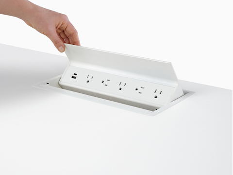 Hand opening an embedded table power source with USB-A port, USB-C port, and five A/C power outlets. Hand opening an embedded table power source with USB-A port, USB-C port, and five A/C power outlets.