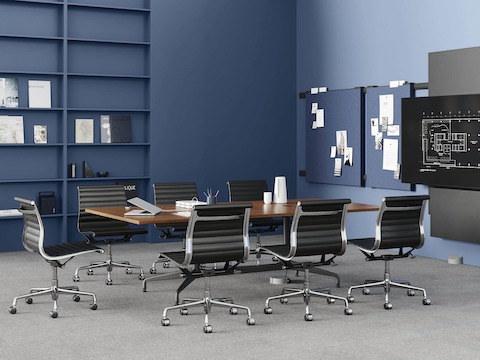 A meeting space with a dark wood conference table and seven black leather Eames Aluminum Group chairs. A Logic Reach Wall Start and Electrical Hub connect the table to power and data.