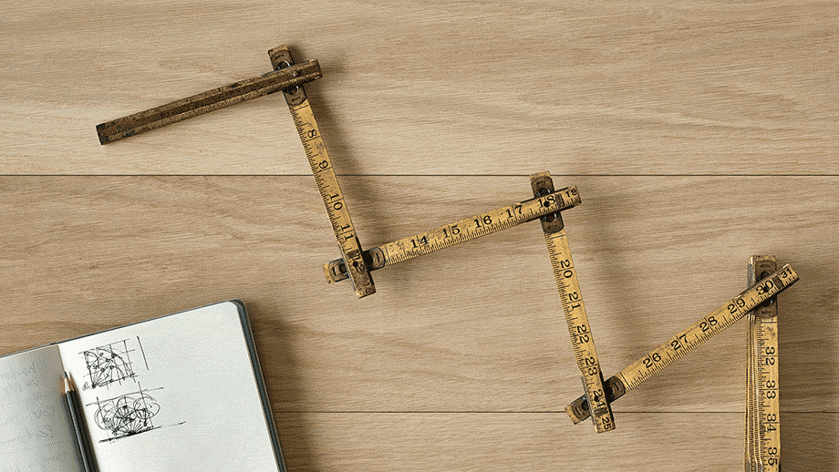 An animated gif showing an overhead view of an antique folding ruler articulating back and forth on one of its hinges, next to an open sketchbook with a pencil in it, all on a light wood surface.