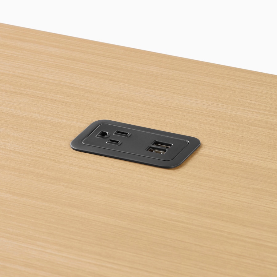 A close-up view of a black power access outlet in a light wood work surface.