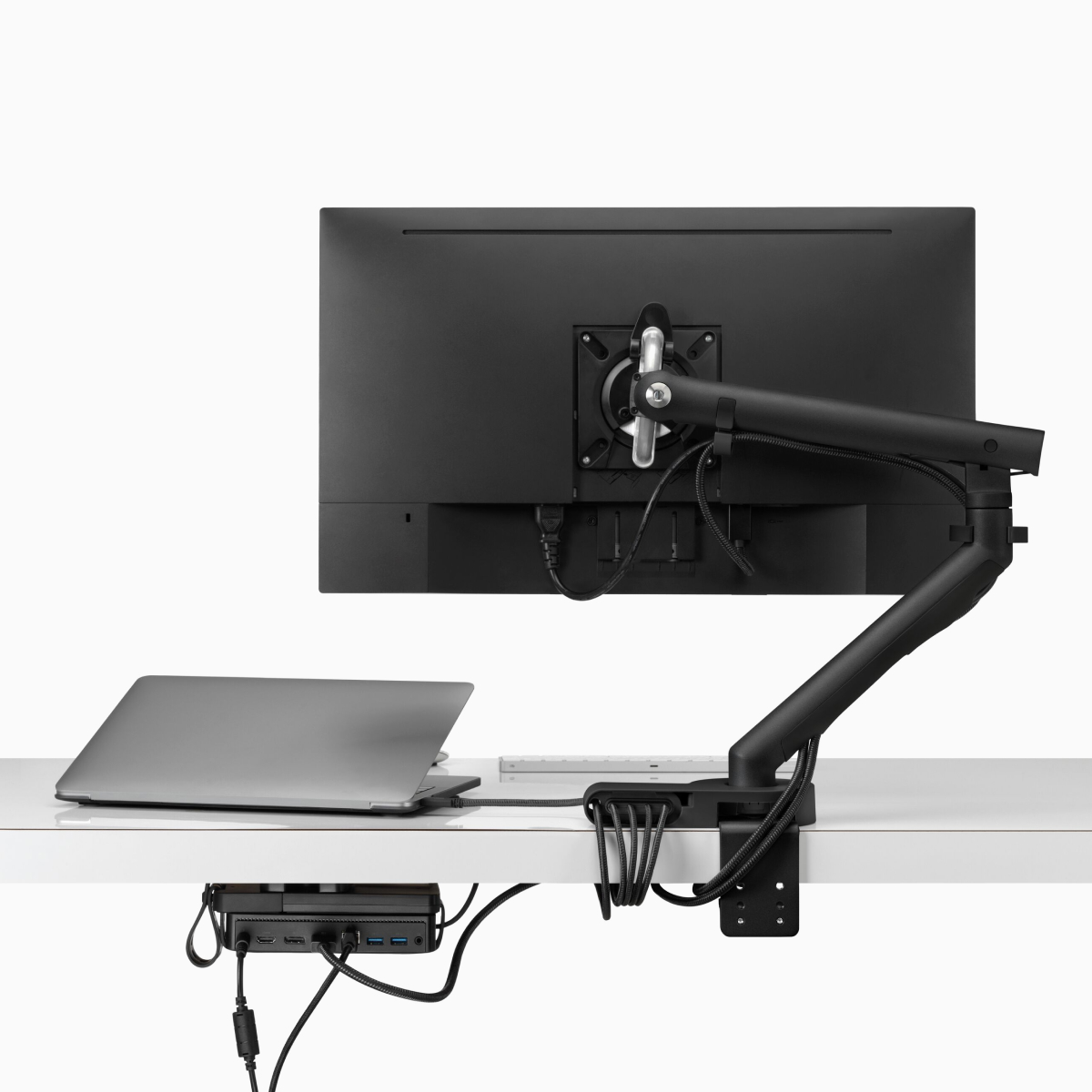 Vista posterior de una pantalla de monitor cuyos cables de energía y datos se conducen desde el brazo articulado para monitor conectado, a través del módulo de conectividad Ondo y el micro soporte en forma de bucle debajo del escritorio.