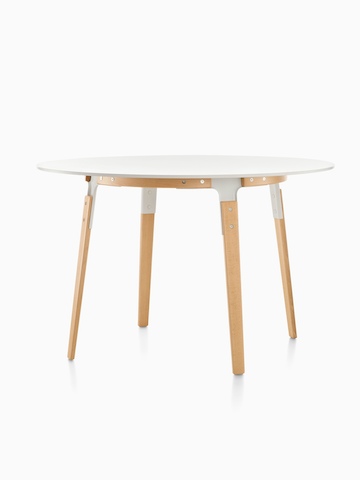 A round Magis Steelwood Table with a white top and wood legs in a light finish.