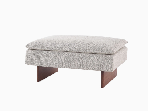 Angled view of a Mantle Ottoman upholstered in Capri Stone with a Walnut Wood Base.