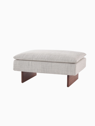 Angled view of a Mantle Ottoman upholstered in Capri Stone with a Walnut Wood Base.