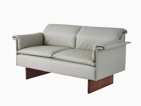 Visão angular de um sofá de dois lugares Mantle estofado em Rhythm Khaki com uma base em madeira de carvalho.