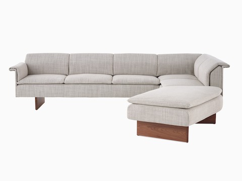Vista en ángulo de un sofá de tres asientos Mantle tapizado en cuero Bristol gris ceniza con base de madera de nogal.