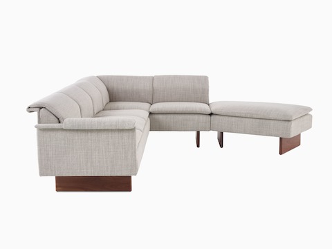 Sofá de tres asientos Mantle combinado con un descansapies Mantle en tapicería Capri Stone con base de madera de nogal.