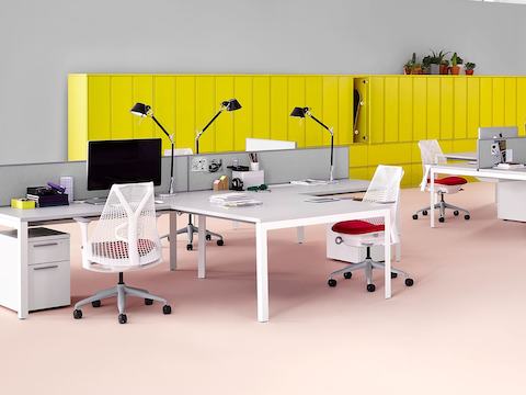 Dos estaciones de trabajo Layout Studio en blanco y gris con sillas Sayl en rojo y blanco y archivos laterales de almacenamiento Meridian y casilleros al fondo en amarillo.