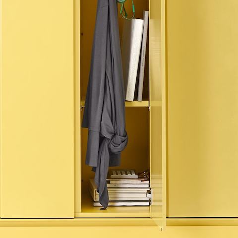 Archivo lateral de almacenamiento Meridian en amarillo con casilleros encima, con una chaqueta, libros y carpetas en uno de los casilleros.
