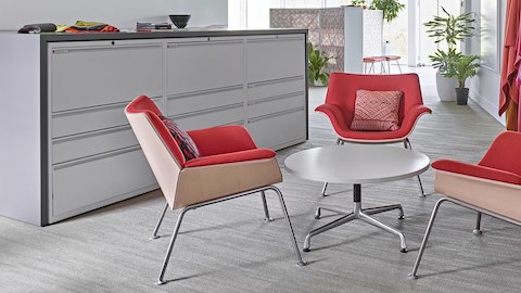 Three white Meridian storage units divide an open work environment. Three pink chairs surround a small white coffee table. Large colourful pieces of fabric hang from racks along the wall. 