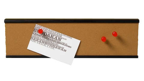 A narrow tackboard with a note and three pins attached.