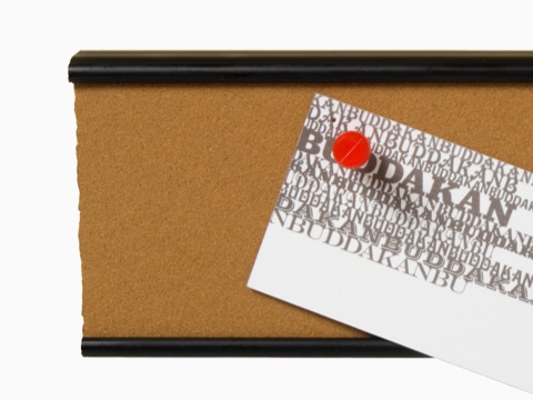 A narrow tackboard with a pin and note attached.