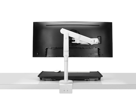 Uma visão lateral de um suporte sit-to-stand Monto em posição fechada e acompanhado de uma tela preta em um braço para monitor Ollin branco com uma presilha estendida.