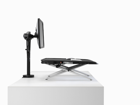 A back angled view of Monto Sit-Stand Riser paired with a black curved screen and Ollin Monitor Arm.