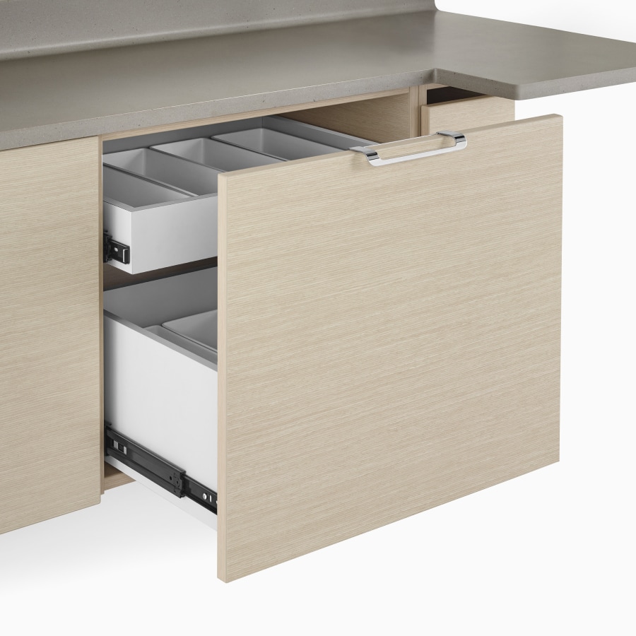 A close-up view of a Mora Casework drawer with storage containers inside and a taupe solid surface top.