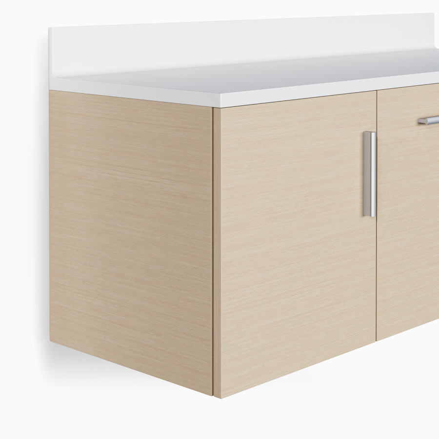 A close-up view of Mora Casework wall-mounted storage in an ash wood finish with a white solid-surface countertop and integrated backsplash.