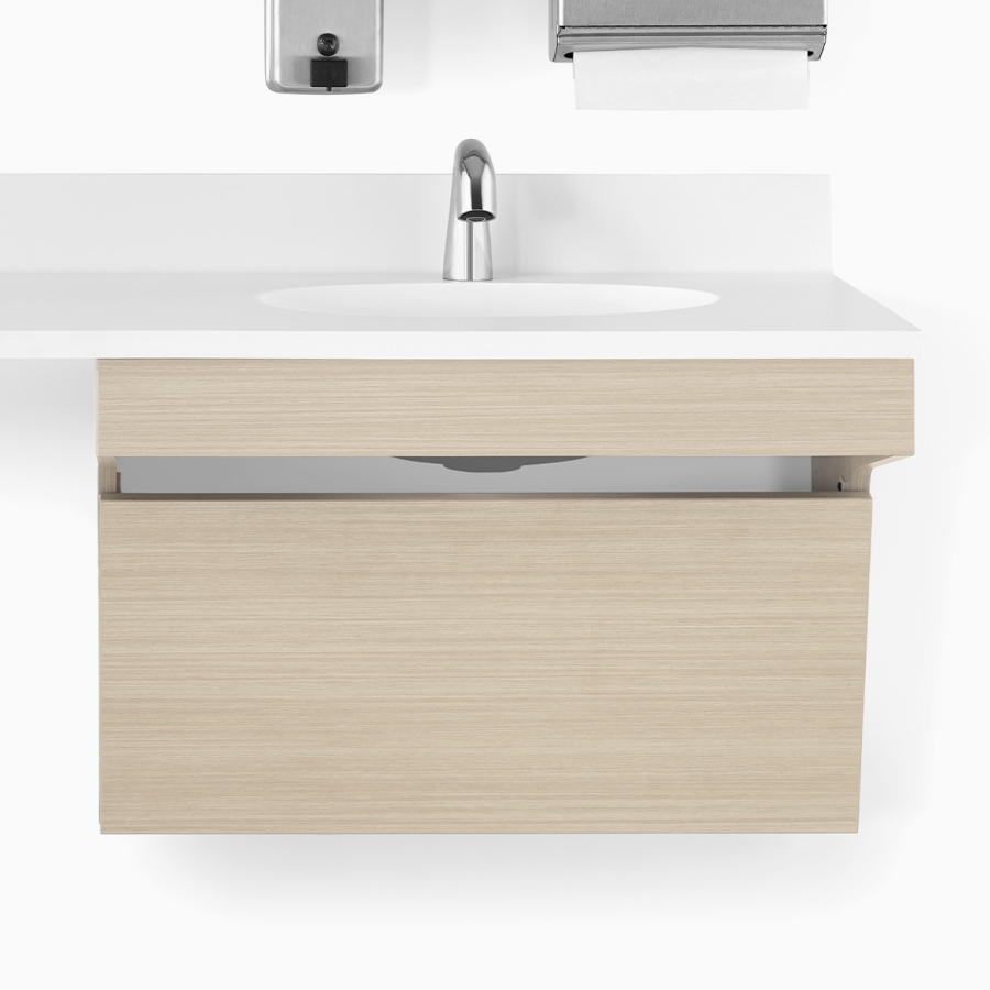 A close-up view of a Mora Casework ADA sink enclosure in an ash finish with a white solid surface top and ADA sink.