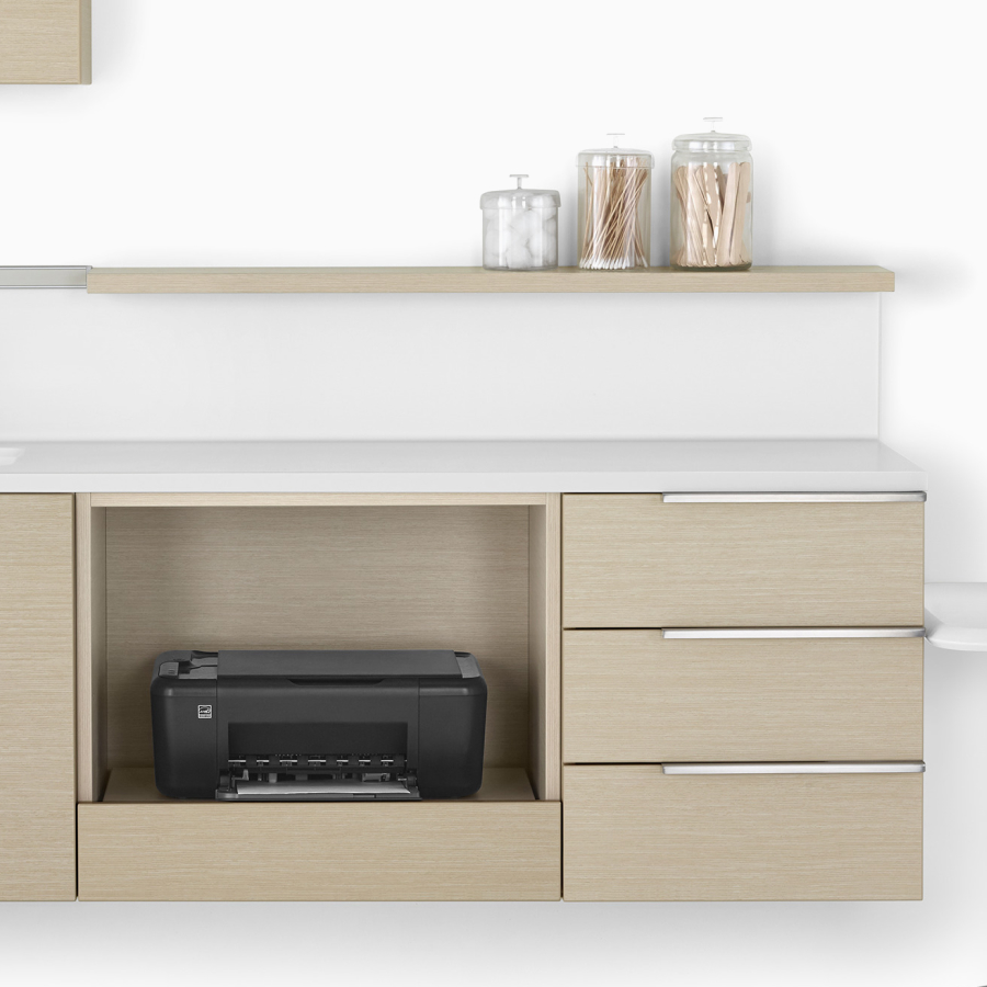 Mora Casework in an ash finish with lower wall-hung storage and drawer cabinets, a white surface, and a floating shelf.