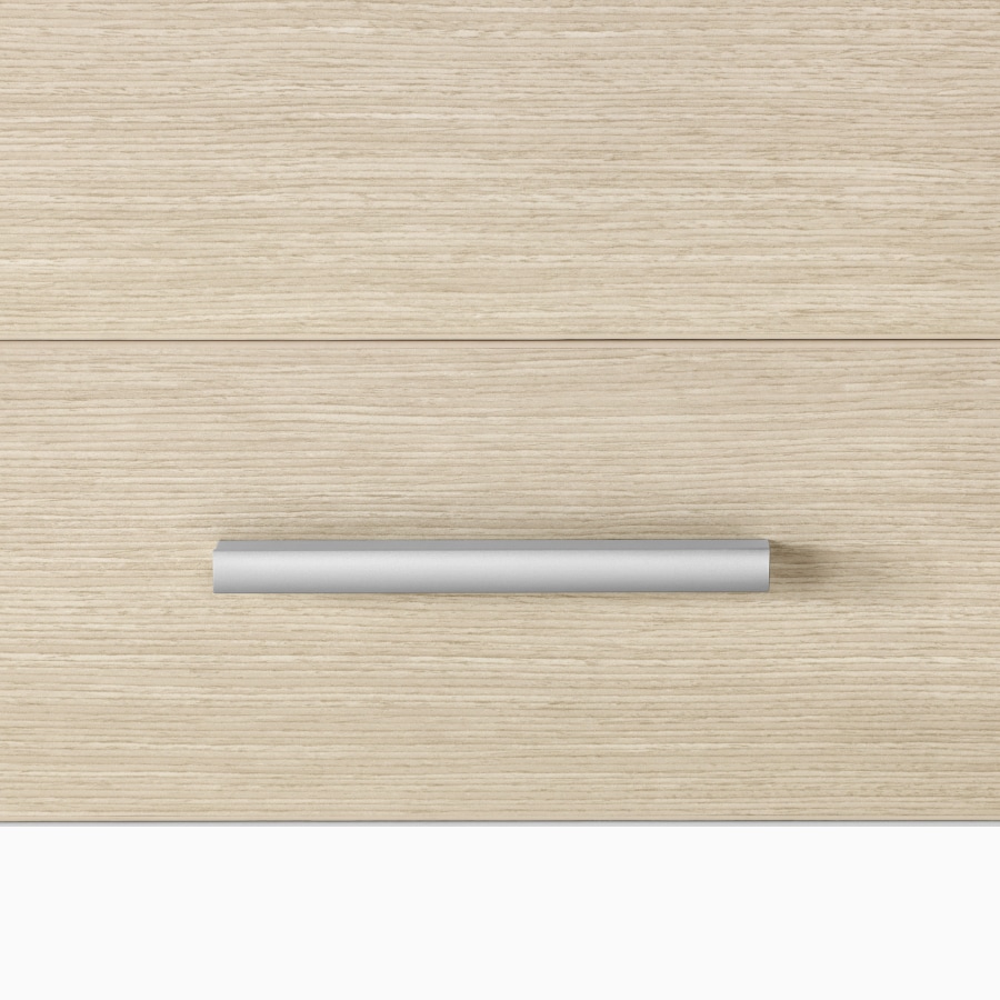 A close-up view of a Mora Casework profile pull in a silver finish on storage in an ash wood finish.