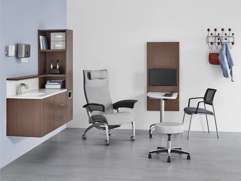 An exam room setting with Mora System casework on the wall in a dark brown finish, and an Intent Solution table located between a patient chair and side chair.
