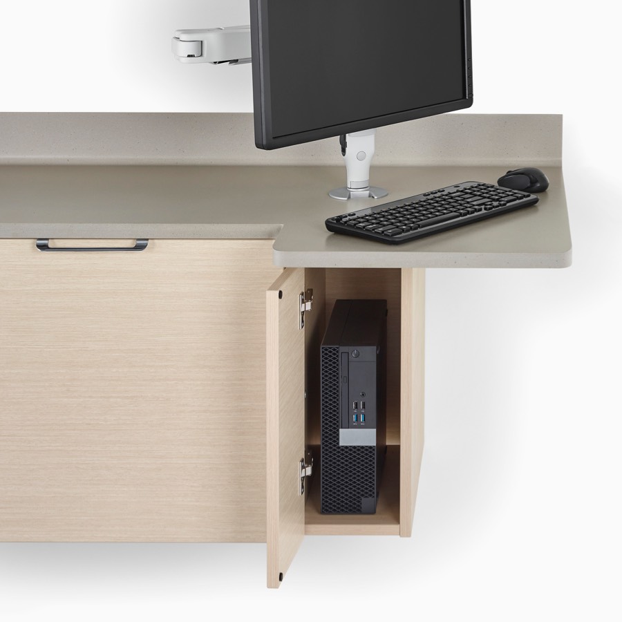 A close-up view of a Mora System casework technology storage cabinet in an ash finish holding a black CPU, and a taupe solid surface top with a monitor support, monitor, and keyboard.