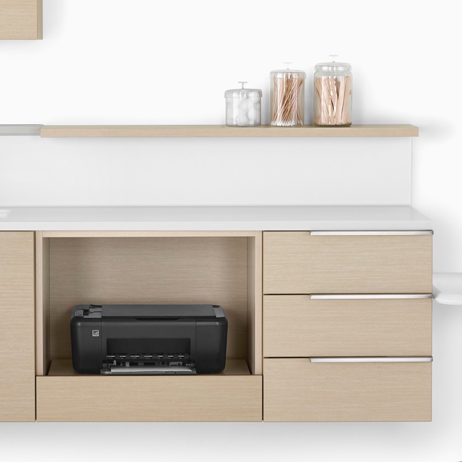 Mora System casework in an ash finish with lower wall-hung unit containing a printer storage cabinet, drawer cabinets, and a sink and surface in white.