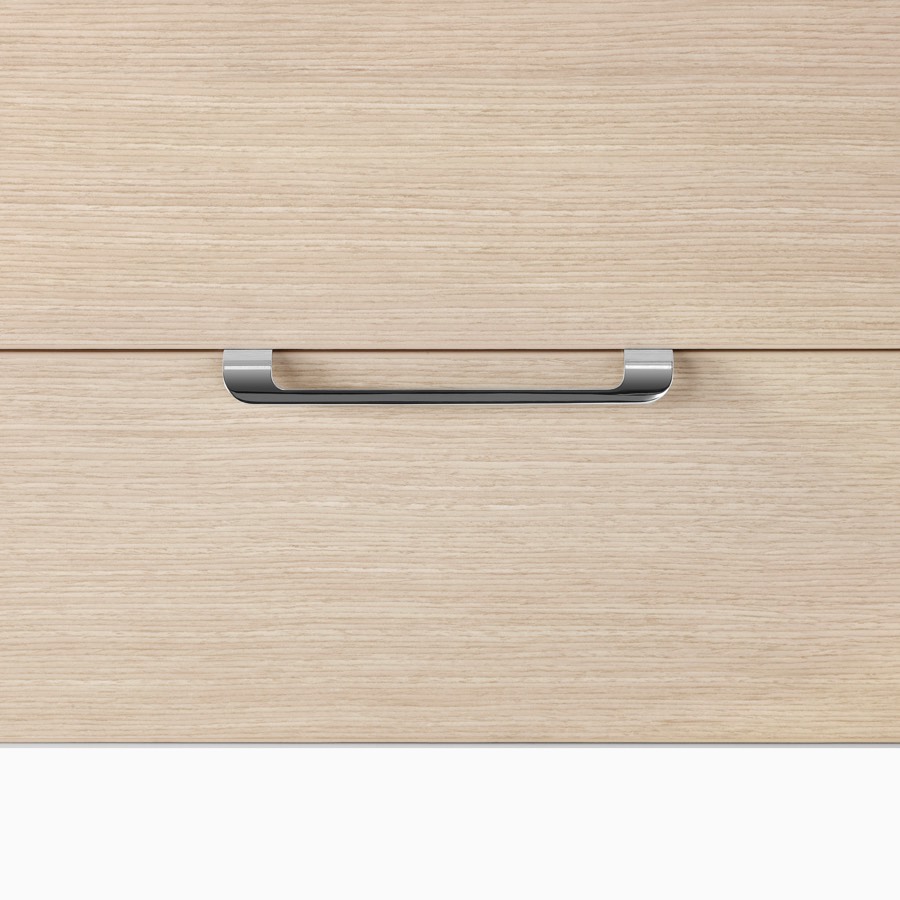 A close-up view of a curved pull on a Mora System casework storage drawer in an ash wood finish.