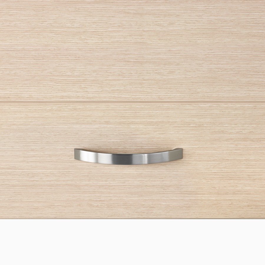 A close-up view of a Mora System casework arc drawer pull in a silver finish on storage in an ash wood finish.
