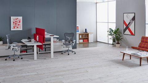 Una estación de trabajo Canvas Channel para cuatro personas con almacenamiento inferior, mesas Motia Sit-to-Stand, pantallas en tela gris y sillas Aeron en gris oscuro.