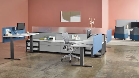 Un espacio de trabajo con cuatro mesas Motia Sit-to-Stand, con tapa superior en blanco, base en negro y pantallas de privacidad integradas con Canvas Office Landscape.